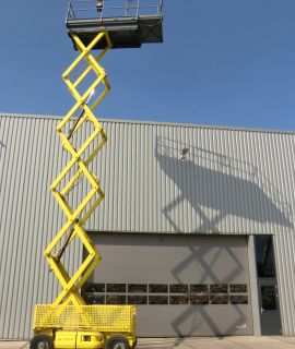 Žlutý nůžkový výtah před průmyslovou budovou.
