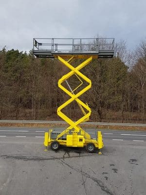 Yellow scissor lift on the road next to the forest